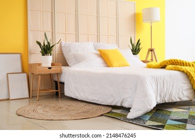 Comfortable bed, folding screen, nightstand, houseplants and blank posters near color wall