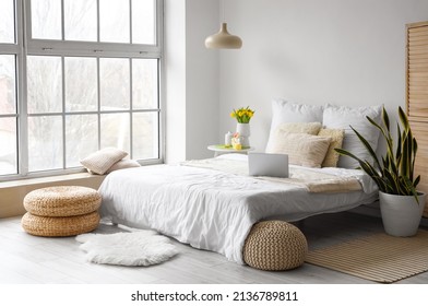 Comfortable bed with laptop, vase with tulips and Easter decor on table in bedroom interior