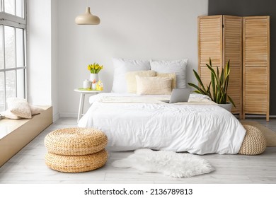 Comfortable bed with modern laptop, vase with tulips and Easter decor on table in bedroom interior