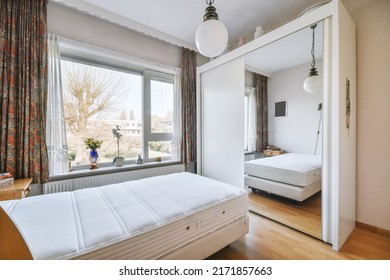 A comfortable bed near a glass bed next to a window and opposite a wardrobe with a mirror in a bright bedroom