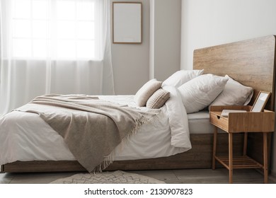 Comfortable Bed And Nightstand With Blank Frame Near Light Wall