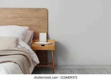 Comfortable Bed And Nightstand With Blank Frame Near Light Wall