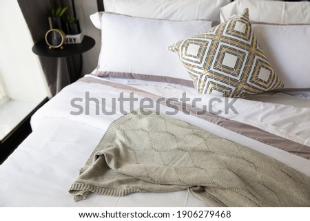 Comfortable bed with soft pillows, bed sheet, knitting blanket. Decorated with matal loft table, clock, small plants and beutiful design of lamp. Bedroom in a modern apartment.