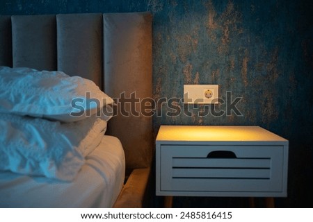 Comfortable bed with stylish bedside table and modern socket with touchpad light switch.