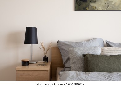 Komfortables Bett mit stylischem Holztisch mit schwarzer Lampe, schwarzer Vase mit dekorativem Gras, gepflegter schwarzer Behälter und Schmuckkasten aus Glas