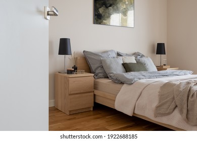Comfortable bed with two wooden bedside tables with decorations and black lamps in simple and cozy bedroom with open doors