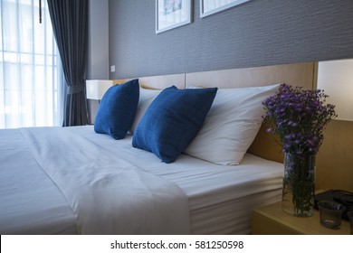 Comfortable Bedroom With  White Bed Sheet, Blue Pillows And Turn Light On Table Lamp 