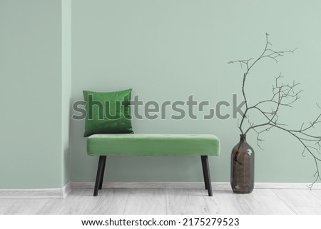 Comfortable bench with pillow and tree branches in vase near light green wall