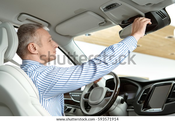 Comfortable car. Mature businessman sitting in a\
car at the dealership adjusting rearview mirror copyspace comfort\
business buying a car driving driver travel auto vehicle luxury\
consumerism concept