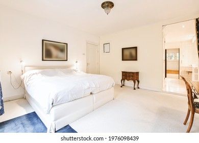 Comfortable Contemporary Bed Located Near Retro Cabinet And Chair In Light Bedroom With Bathroom Doorway At Home