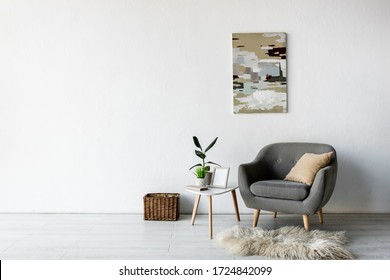 comfortable grey armchair near coffee table with green plants and frame in modern living room