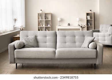 Comfortable grey couch in cozy empty living room. Modern Scandinavian interior with stylish sofa, cushions, cozy home decoration, elegant furniture in background. Real estate apartment for rent, sale
