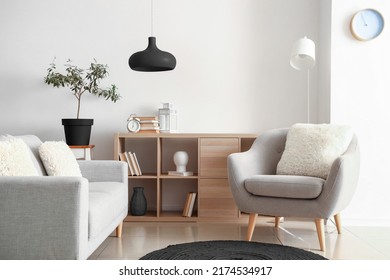 Comfortable grey furniture with wooden shelving unit and black lamp in light living room - Shutterstock ID 2174534917