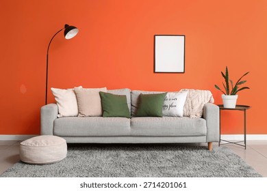 Comfortable grey sofa with soft pillows and floor lamp near orange wall in living room