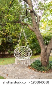 Comfortable hanging wicker white chair in summer garden. Cozy hygge place for weekend relax in garden. Hammock chair in boho style hanging on tree. Cozy exterior backyard. Concept of rest outdoor. 
