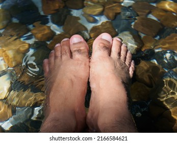 Comfortable Holiday Soaked His Bare Foot In The Stream. 
Couple Foot Dipped In Serene Lake Transparent Water With Pebbles.