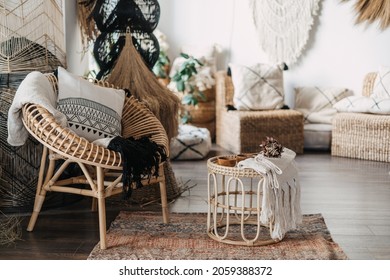 Comfortable living room with ethnic interior design in bohemian style. Apartment with home decor, rattan furniture, armchair with cushions, bamboo coffee table, carpet on wooden floor