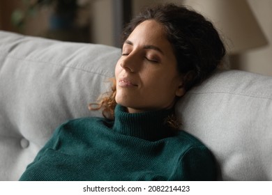 Comfortable rest. Calm millennial latina woman taking break for relax sitting on couch breathing deep working on emotional control meditating. Tranquil young lady napping dreaming keeping eyes closed