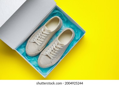 Comfortable shoes in cardboard box on yellow background, top view. Space for text