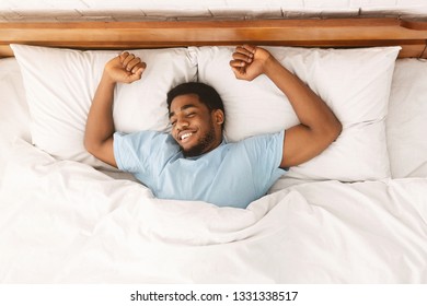 Comfortable sleep. Smiling african-american millennial guy sleeping, sprawled in bed, top view