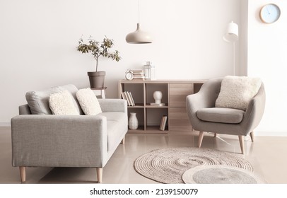 Comfortable sofa, armchair and shelf unit with decor near white wall in room interior