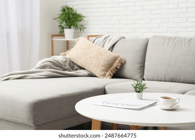 Comfortable sofa and coffee table with magazine and cup of tea in living room