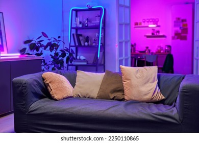 Comfortable sofa with row of soft cushions standing in the center of living room lit with neon light prepared for guests and home party