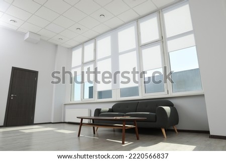 Comfortable sofa and table near large window with white roller blinds indoors