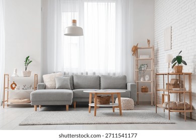 Comfortable sofa and table near window with white curtains in interior of living room