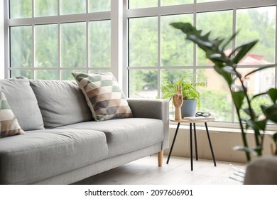Comfortable sofa, table with wooden hand and houseplant in room with big window