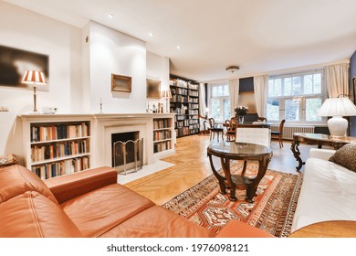 Comfortable sofas and round table located near fireplace with bookshelves in elegant living room in house