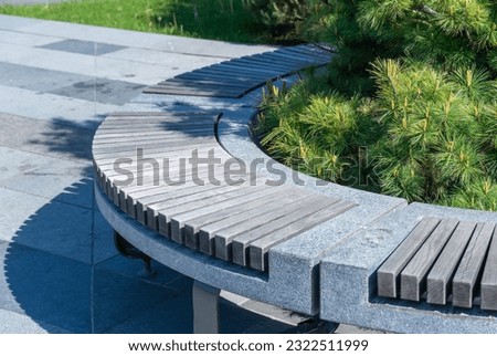 Comfortable in stone and wooden material bench in city park. Design of gray and brown stationary seat for leisure. Geometry on nature and place to rest. Exterior empty park bench. Furniture in garden.