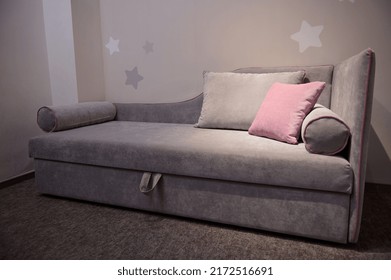 Comfortable velour sofa bed with pillows for children room displayed for sale in upholstered furniture store against gray wall background. Cozy home interior, home design project
