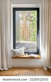 A comfortable window seat features a soft pillow and an open book. Cozy reading nook by the window in bedroom with decorative cushion and peaceful view in the forest, vertical shot