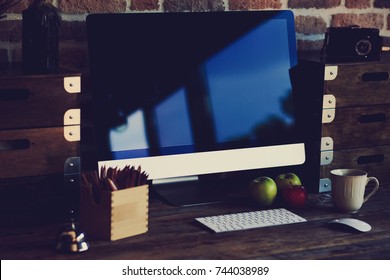 Comfortable workplace with big computer screen, mouse and keyboard. Wooden table with pencils for drawing and colorful apples.  Desktop with  cup of coffee and fresh apples for healthy breakfast.