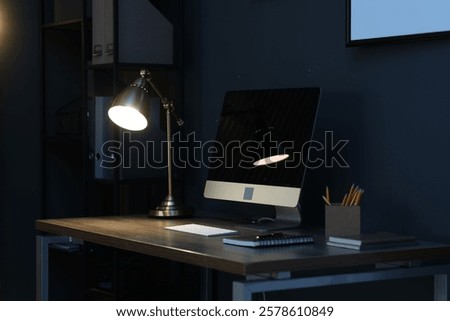 Comfortable workplace with computer and lamp on wooden desk at home office in evening