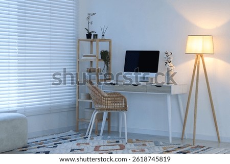 Comfortable workplace with computer on desk and floor lamp at home office in evening