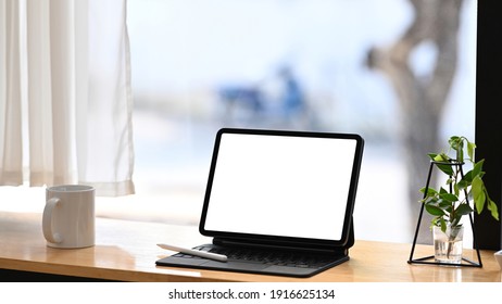 Comfortable workplace with computer tablet, coffee cup and plant on wooden table.