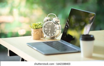 Comfortable Workplace, Office Desk With Blank Screen Laptop And Clock, Plant, Nature Light Bokeh Background. Startup At Work In The Morning, Coffee Shop, Co Working Space. Copy Space, Vintage