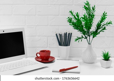 Comfortable Workplace Office - Work Table With Blank White Laptop And Notebook - Home Office With Red Coffee Mug - Office Desk Supplies And Flower On Light Background With Brick Wall