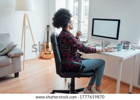 Comfortable workplace. Side view of afro american woman looking at computer screen while working or learning online from home. Home interior. Freelace. E-learning. Distance education. Stay home