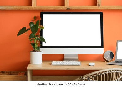 Comfortable workspace with modern computer and anthurium flower near orange wall, closeup