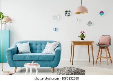 Comfy sofa, coffee table, pouf, wooden table and chair, and hanging patterned plates in a sweet living room interior - Shutterstock ID 1090132580