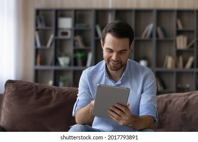 Comfy working on pad. Focused millennial guy student enjoy using digital tablet at home scroll information on touchscreen read electronic document. Smiling young man user hold tab computer pc surf web