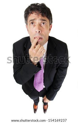 Comic portrait from a high perspective of a forgetful or ignorant businessman standing with his finger clasped between his teeth and a worried expression, isolated on white