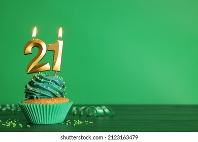 Coming of age party - 21th birthday. Delicious cupcake with number shaped candles on green wooden table, space for text