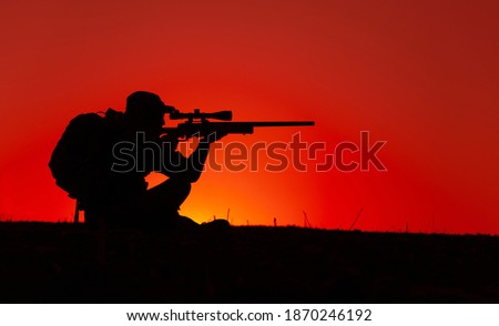 Commando team sniper, army special forces shooter aiming, shooting sniper rifle while sitting on sea or ocean shore during sunset. Coast or border guard soldier observing coastline with optical sight