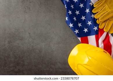 Commemorating the significant contributions of construction workers on American Labor Day. Above shot of flag, helmet and gloves on grunge textured grey concrete. Suitable for ads or text - Shutterstock ID 2338078707