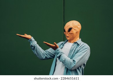 Commercial advice image portrait with green wall background to copywrite and write text and man in showing posture wearing alien ufo mask in casual clothes. Sales and discount adv concept