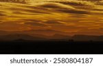 Commercial airliner descends for its final approach and landing in a silhouetted mountainous city under a hazy apocalyptic sky.  